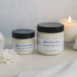 Small and large body butter jars displayed with a candle, two rolled paper towels, and a white flower